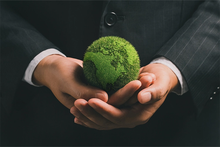 Imagem foca em um globo todo verde, representando vegetação, que está nas  mãos de um homem vestindo terno.