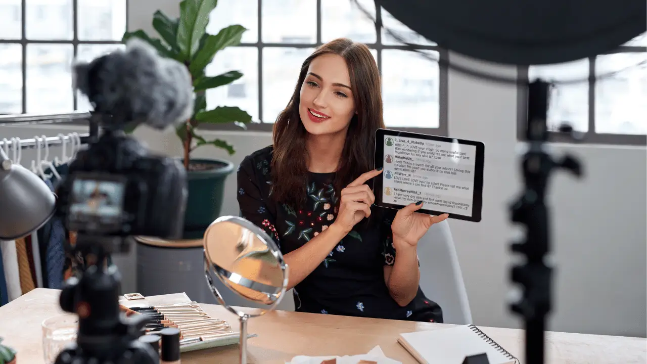 Mulher jovem, branca, falando para uma câmera e mostrando algo em um tablet.