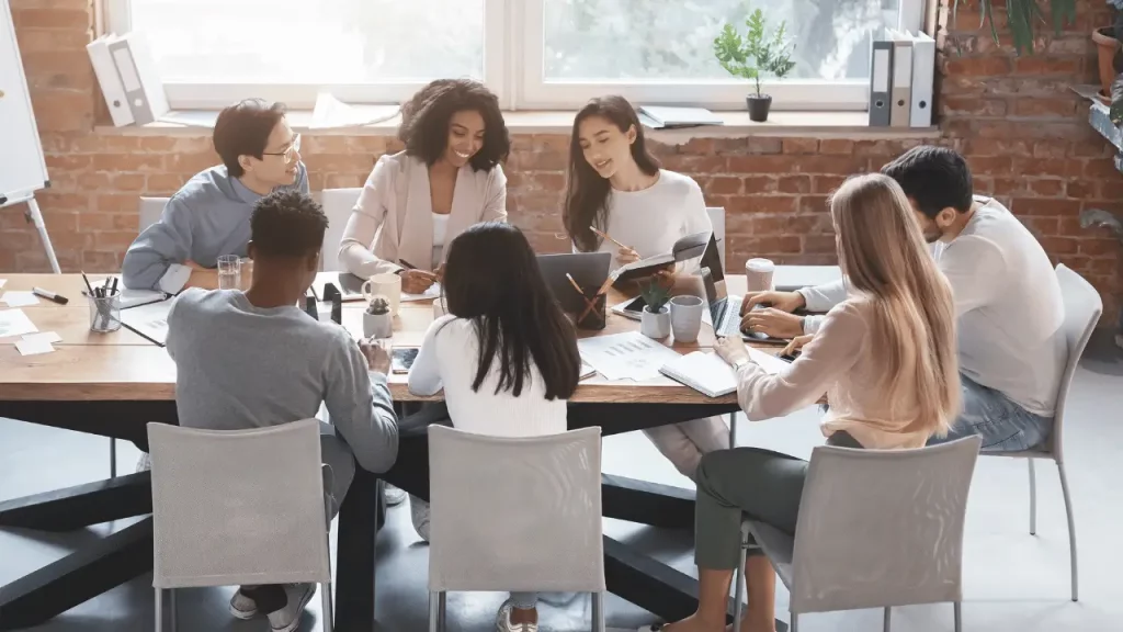 Equipe de trabalho reunida em uma mesa. Há quatro mulheres e três homens. 